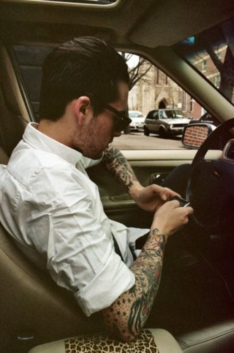 Hombre con tatuajes enviando mensaje de texto por celular