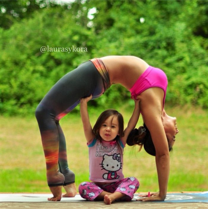 Niña debajo de su madre practicando yoga 