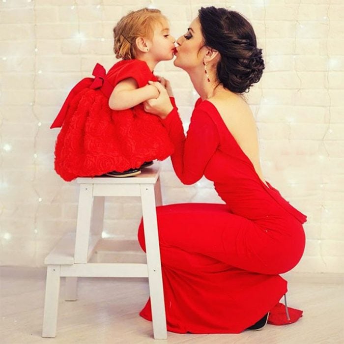 mamá besando a su hija que está arriba de un banquito 
