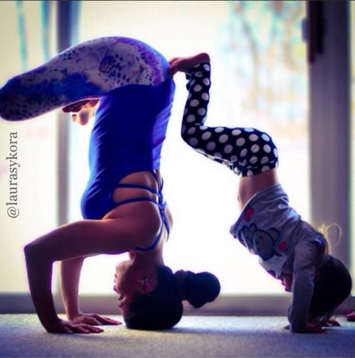 Madre e hija posando un paso de yoga de cabeza una recargada sobre la otra 
