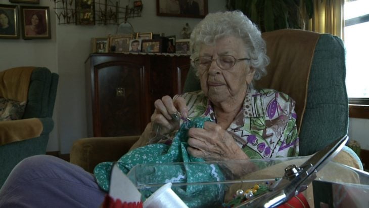 Mujer de 99 años sentada cosiendo un vestido 