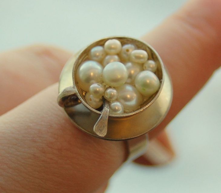 Fotografía de anillo sobre un dedo en forma de taza de capuchino con perlas en la superficie 