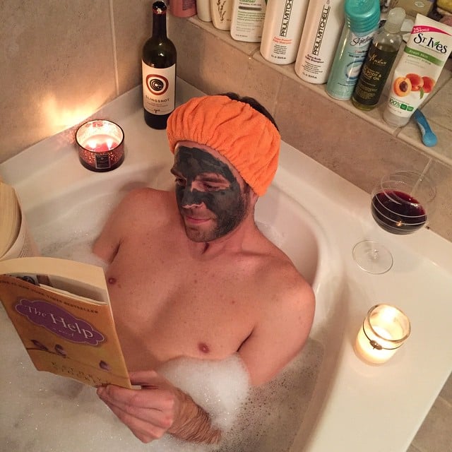 man taking a bath in a tub with aromatic candles and a book