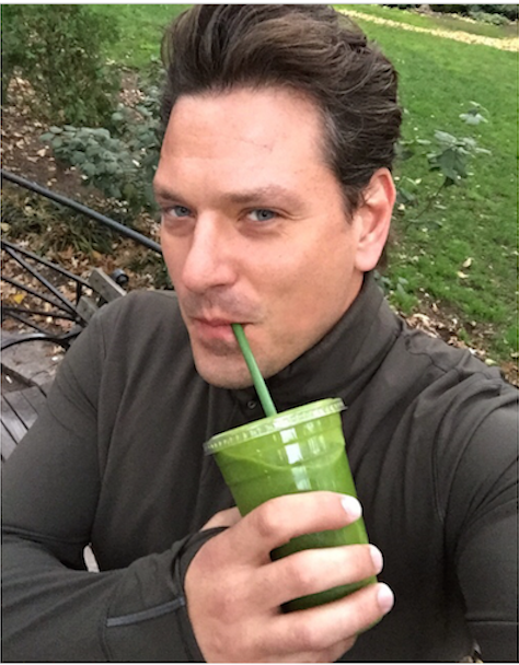 man living a green juice sitting in a park 