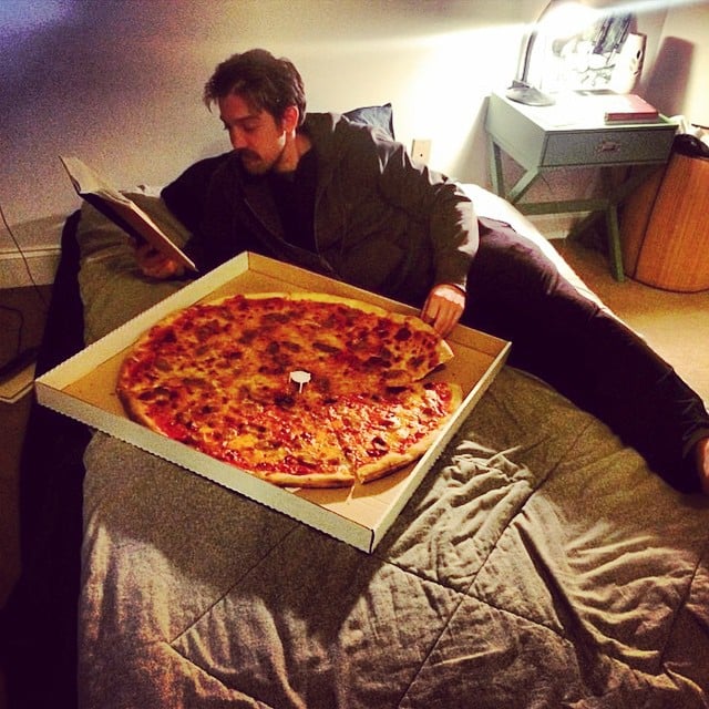man eating pizza in bed 