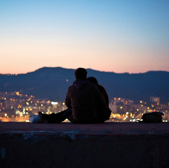 novios sentados viendo la ciudad desde un mirador 