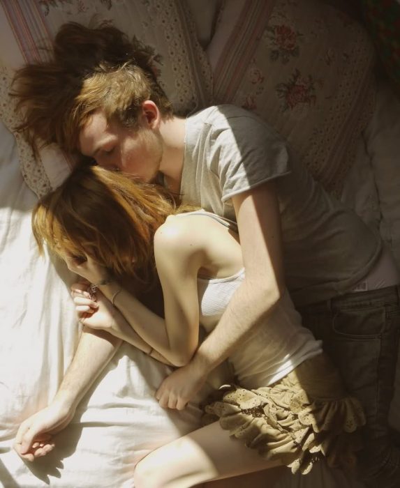 chica abrazada a un chico mientras ambos están recostados en la cama 