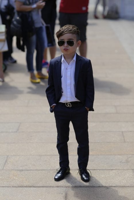 Niño fashionista usando un traje parado en la calle enviando una foto 