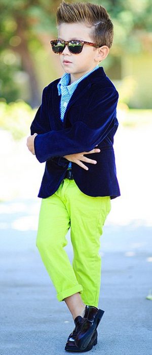 NIño con pantalón neón y saco azul y lentes obscuros posando para una fotografía 