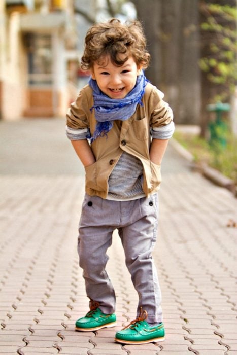 Bebé usando una chaqueta bufanda y pantalón gris parado en la calle 