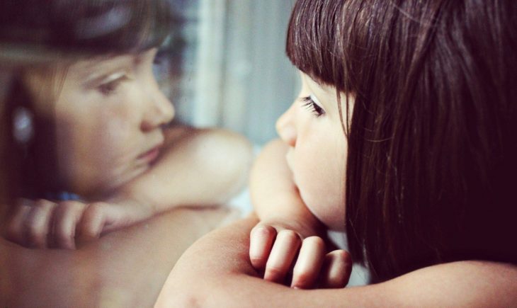 niña mirando su reflejo por la ventana