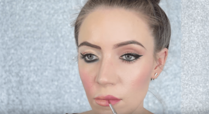 mujer rubia pintandose los labios de color rosa