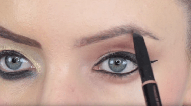 chica de ojos verdes maquillando cejas con pincel