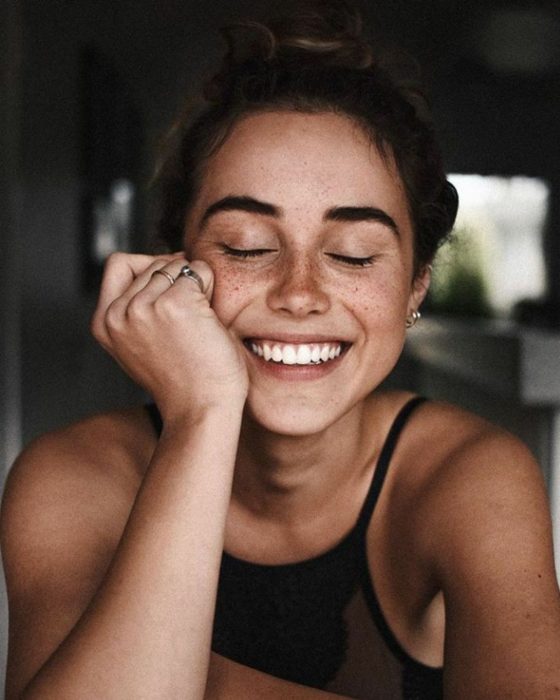 Chica con pecas sonriendo con los ojos cerrados