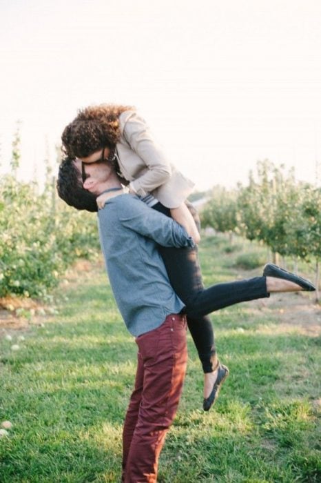pareja de enamorados en medio del campo besándose mientras él la carga 