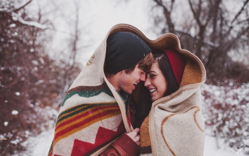 novios abrazados y cubiertos con una manta bajo la nieve 