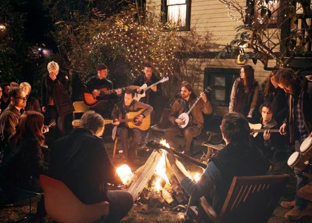 personas al rededor de una fogata tocando la guitarra y cantando 