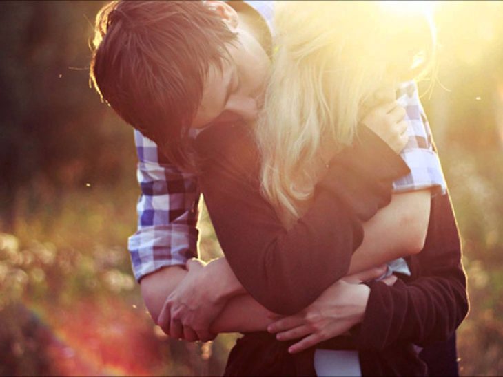 novios abrazados en un campo con la puesta de sol 