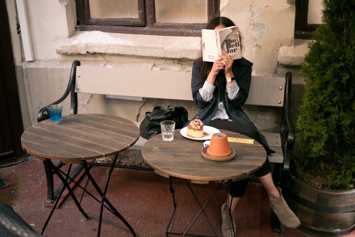 Mujer leyendo en una banca mientras disfruta de un flan y un vaso de agua