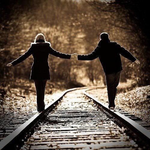 pareja caminando por las vías del tren tomados de las manos 