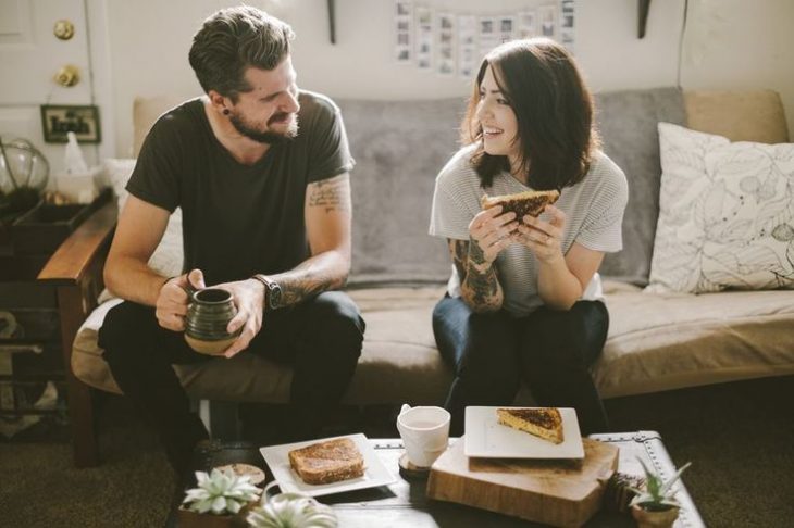 novios sentados en el sillon comiendo y tomando café 