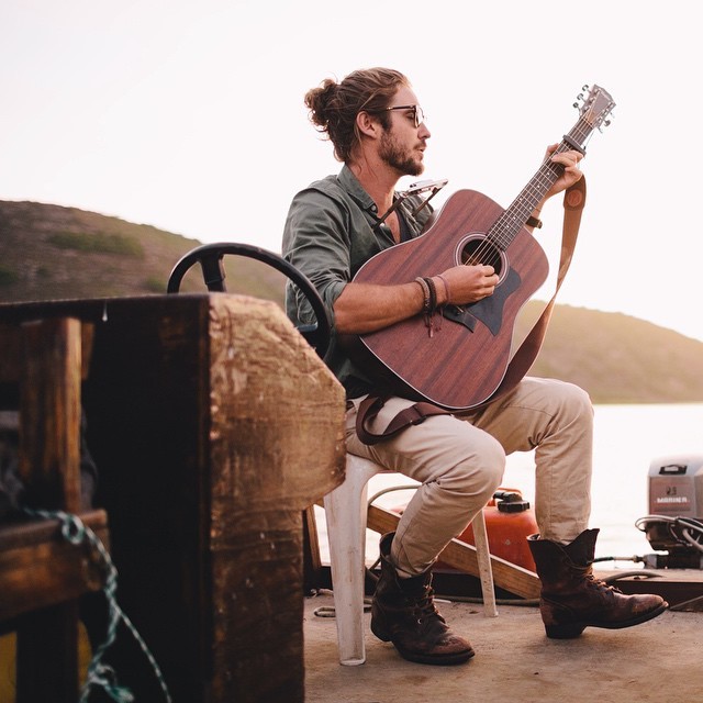 Hombre músico con barba al pie de un lago