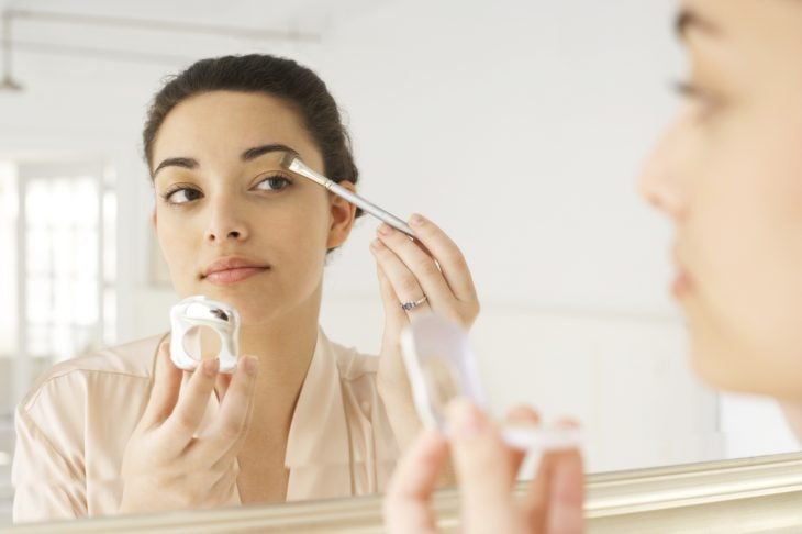 Mujer frente a un espejo pintándose un ojo 