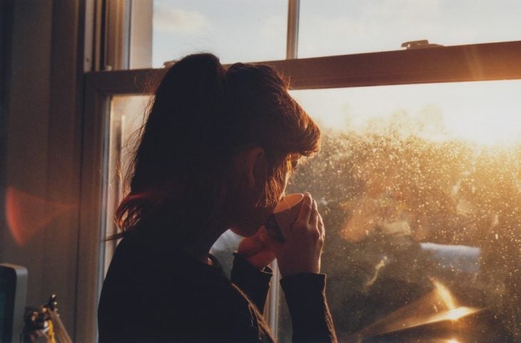 Mujer tomando una taza de café mientras observa por la ventana 