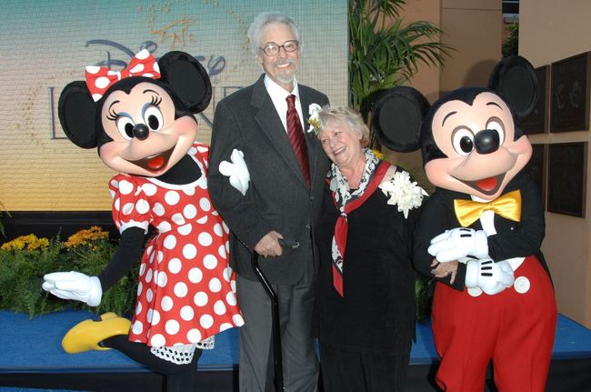 pareja de adultos mayores al lado de los personajes de Disney mimi y mickey mouse 