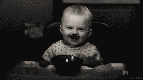 bebe con bigote sentado comiendo de un tazón 