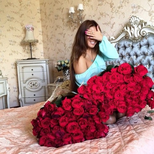 mujer sentada en medio de la cama cargando dos ramos de rosas rojas 