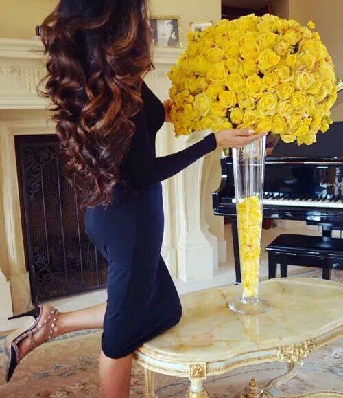 mujer de vestido azul y cabello suelto admirando unas rosas amarillas 