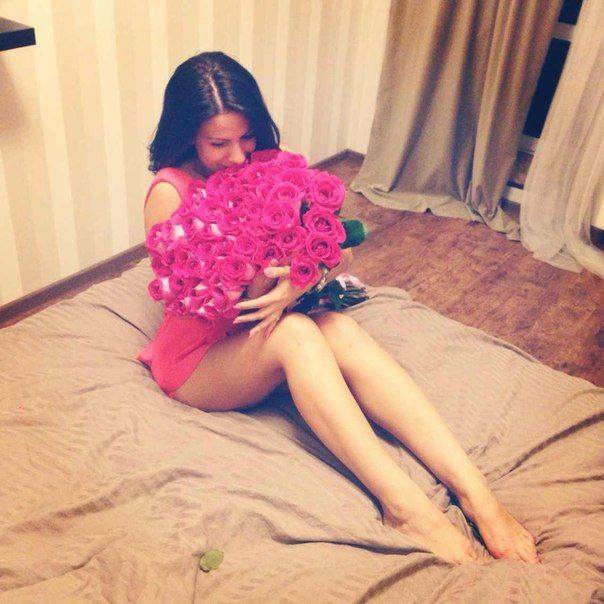 mujer sentada en medio de una cama abrazando un ramo de rosas 