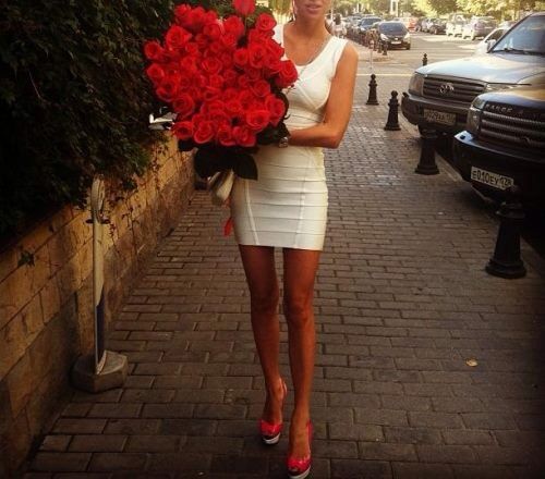 mujer cargando un ramo de rosas rojas vestida de blanco mientras camina por la calle 