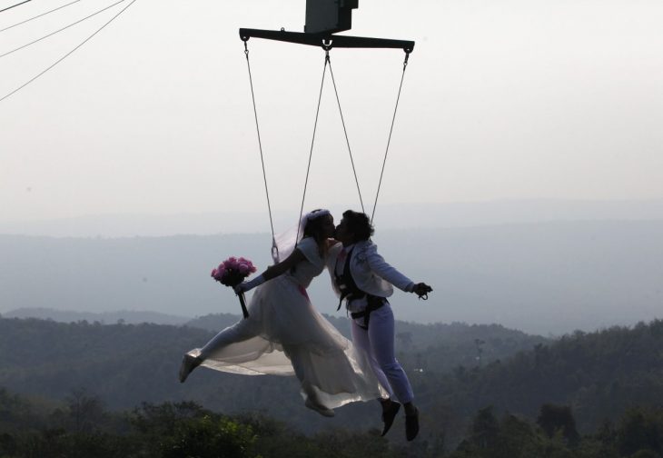 novios suspendidos en el aire sostenidos por cables mientras se besan