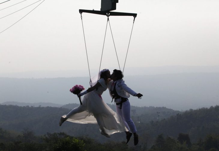 novios suspendidos en el aire sostenidos por cables mientras se besan 