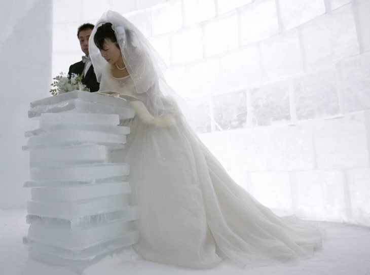 pareja de novios firmando una acta que esta sobre una pila de hielo mientras ellos están en un iglu 