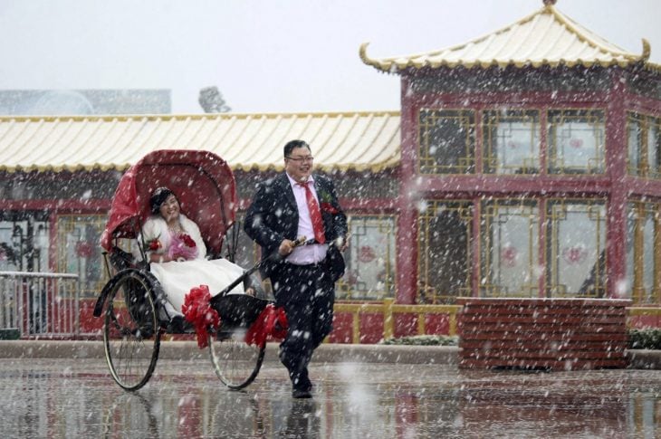 hombre jalando un trineo con su esposa dentro de el mientras esta nevando 