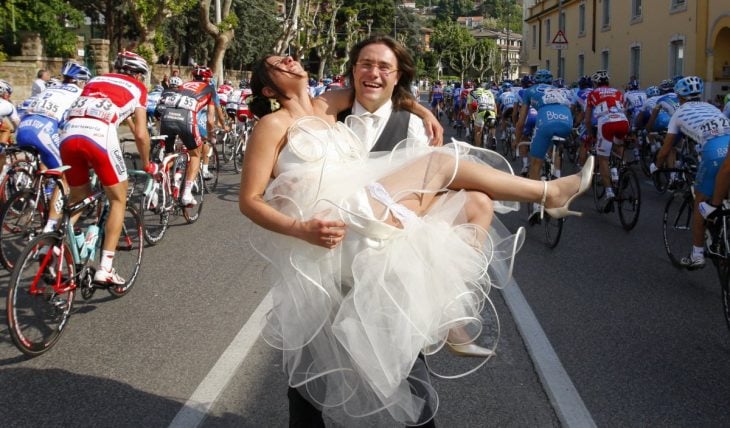 novio cargando a la novia en medio de un maratón de ciclismo 