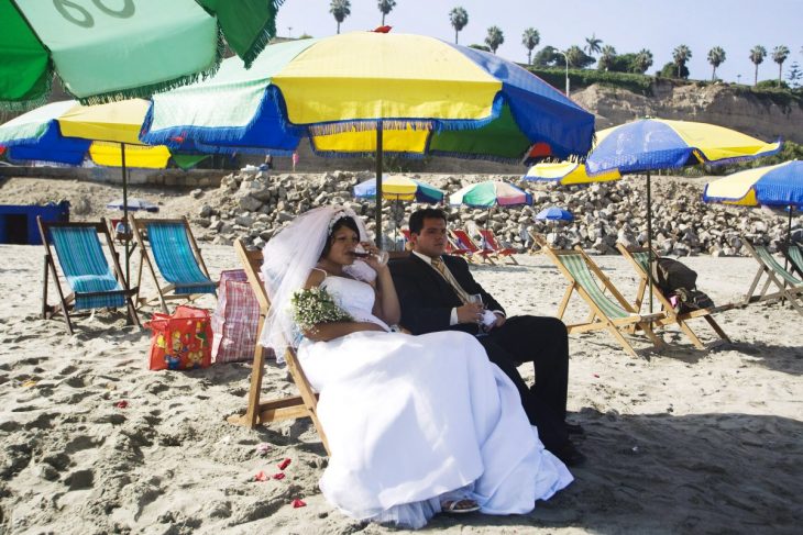 novios sentados en una playa bebiendo vino 