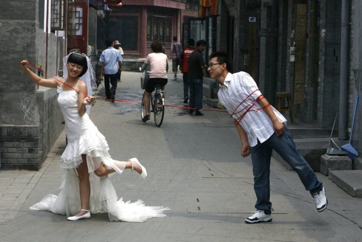 novia atando con un cordón a su novio en un callejón transitado 