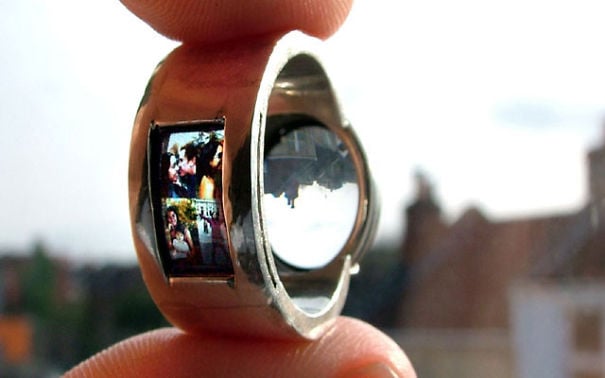 fotografía de manos sosteniendo un anillo con proyector y reflejando una imagen de una pareja 