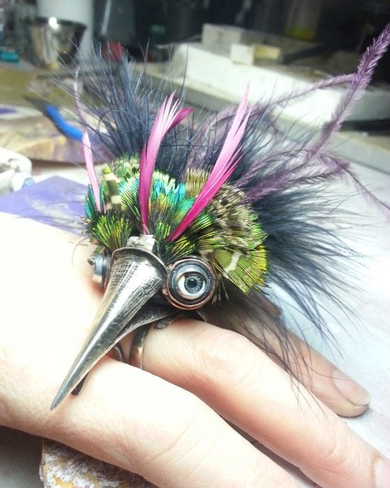 Anillo en forma de pájaro con plumas de colores verde, rosa y morado con grandes ojos y pico 
