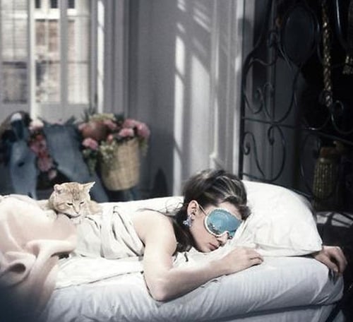 chica acostada en una cama usando un antifas para dormir mientras el gato esta sobre ella 