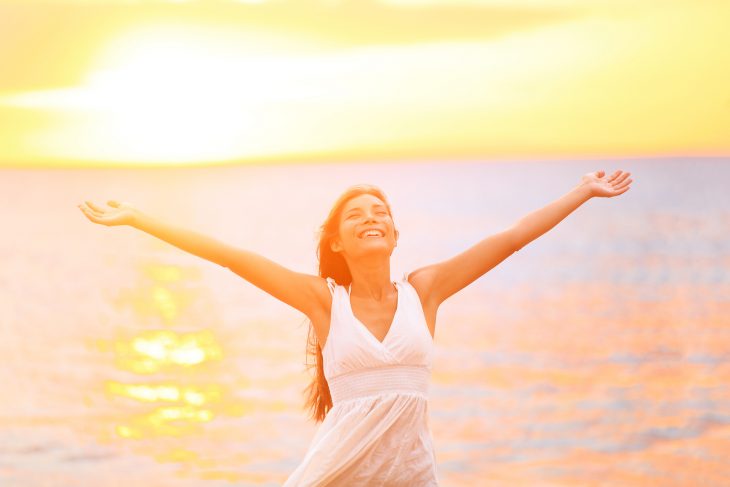 mujer feliz cno los brazos abiertos sonriendo en la playa 