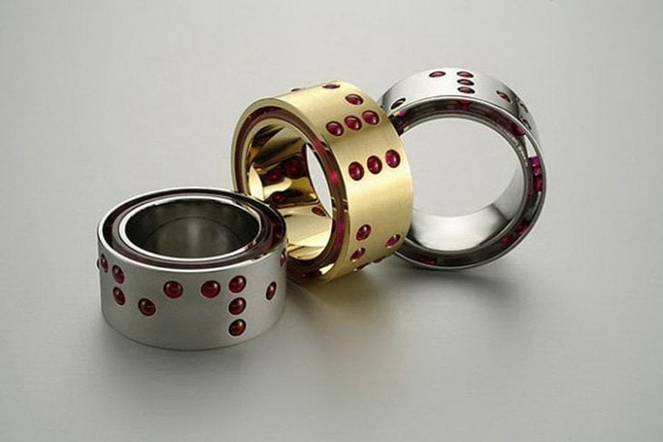 Fotografía de anillos de color dorado y plata con puntos rojos en una superficie plana de color plata 