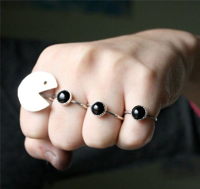fotografía de puño mostrando anillos con forma del vídeo juego Pac-Man en color plata y negro 