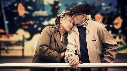 pareja de ancianos recargados en una barandilla besandose 
