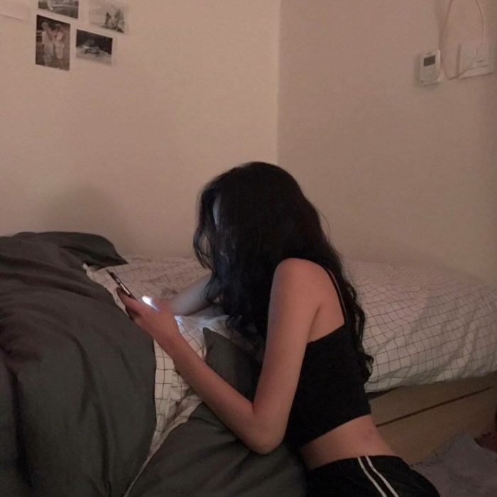 Chica recargada en la cama viendo el celular