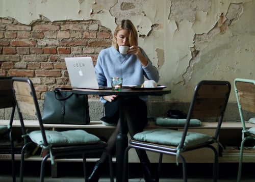 mujer sentada tomando café y revisando su computadora 